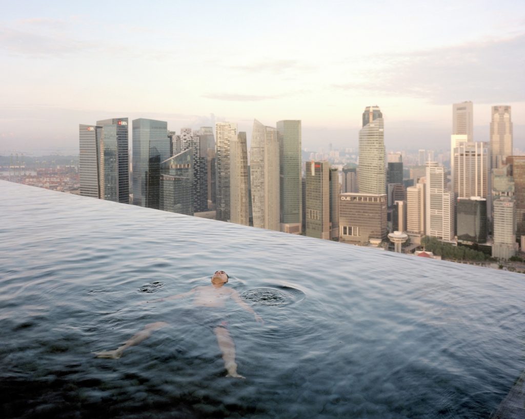 A man floats in the 57th-floor infinity pool with the skyline of Singapore’s financial district behind him. Photo: Paolo Woods and Gabriele Galimberti