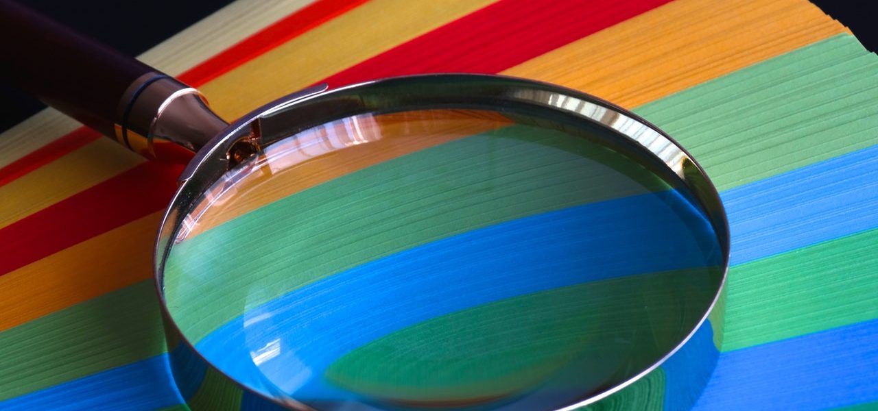 magnifying glass placed on top of colourful papers A magnifying glass placed on top of colourful papers