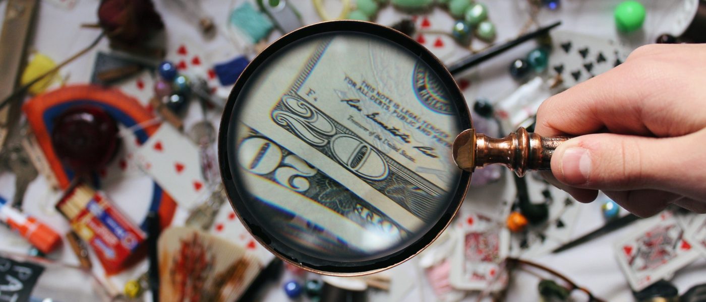 magnifying glass spotting dollar bills amid a mess of objects Magnifying glass spotting dollar bills amid a mess of objects